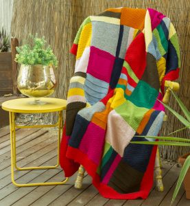 Modern, bright rug with squares and lines in shades of yellow, orange, pink, red, lime, navy, brown, grey and white, with a red trim.